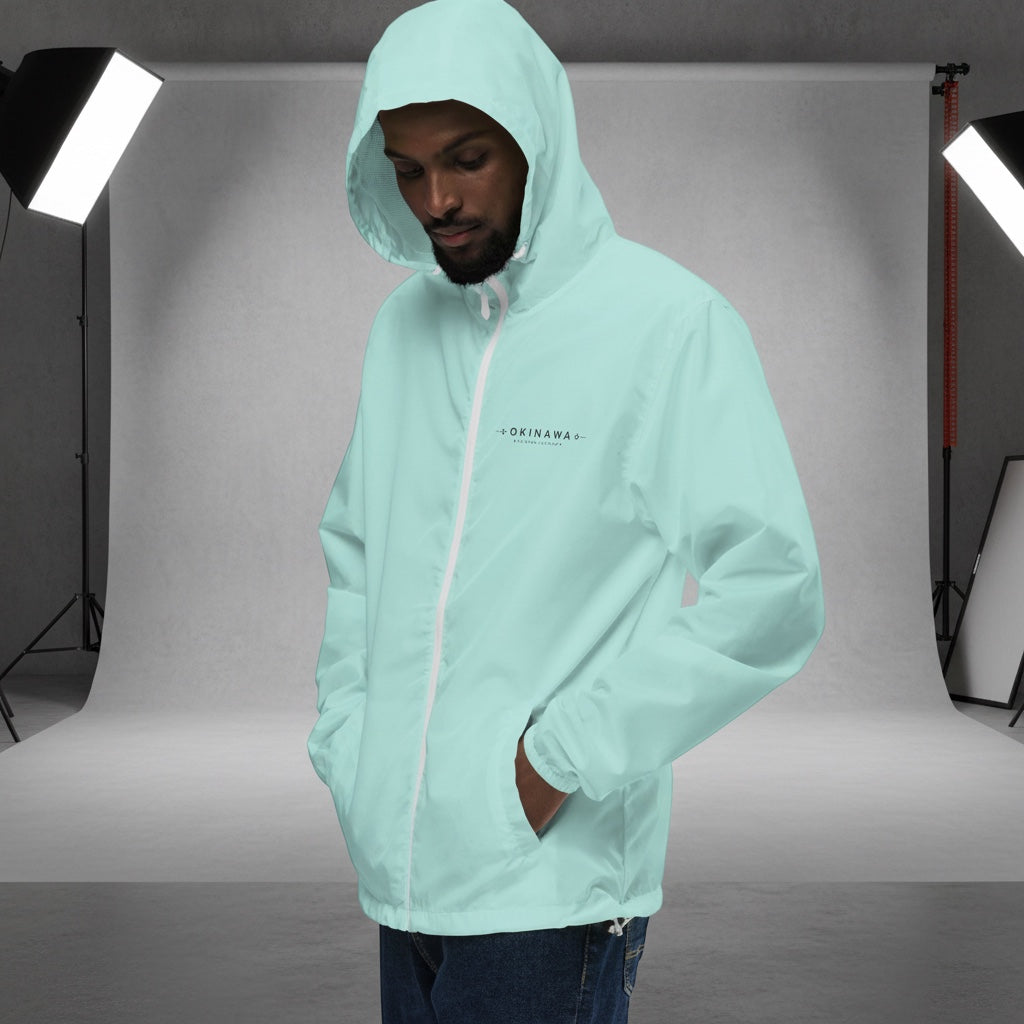 YUTASHA Toshie light blue unisex windbreaker with a hood, white zipper, and Okinawa chest print in a studio setting.