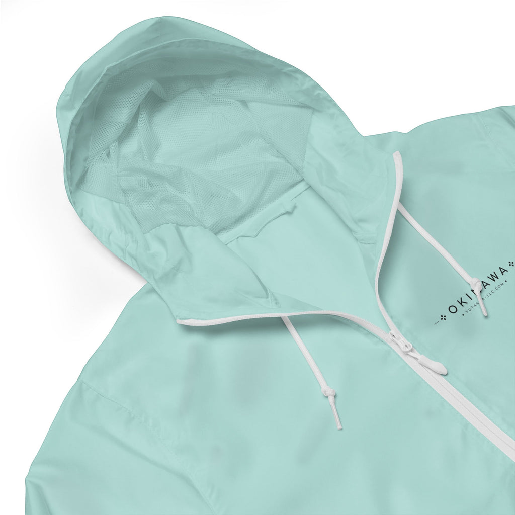 YUTASHA Toshie windbreaker in light mint green with a white zipper, mesh-lined hood, and Okinawa logo detail.